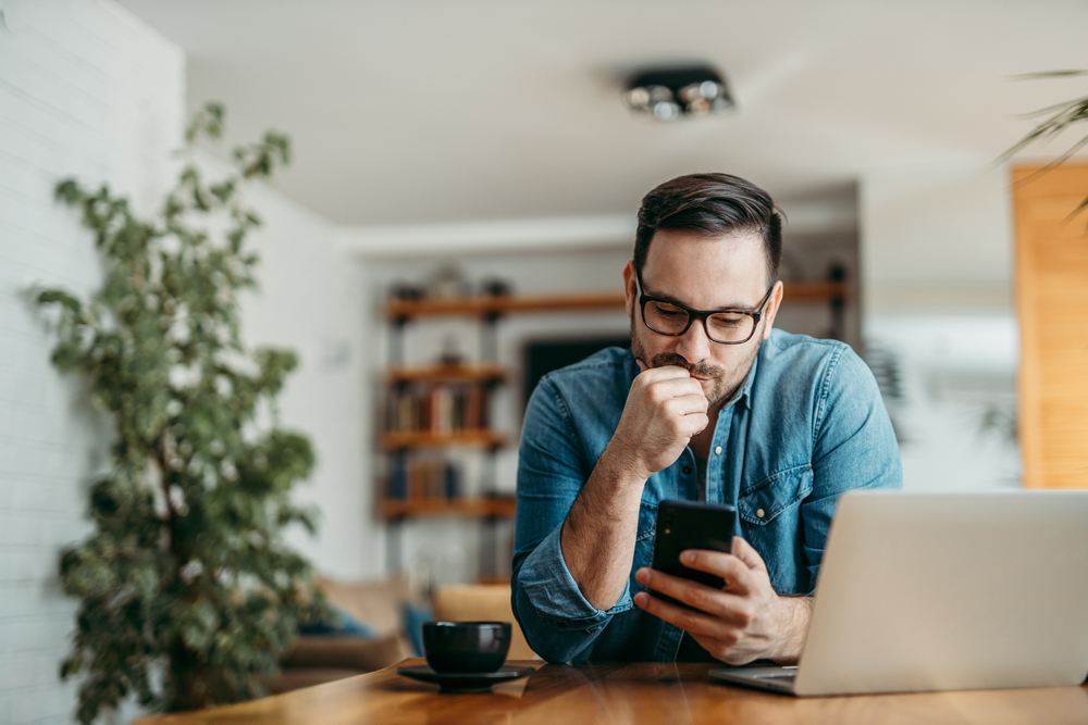 Portrait,Of,A,Puzzled,Man,Looking,At,Smart,Phone,,Sitting
